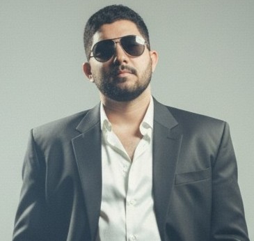Portrait of Mr. Vijay Choudhary wearing a red t-shirt standing in front of a lush green garden with soft evening lights